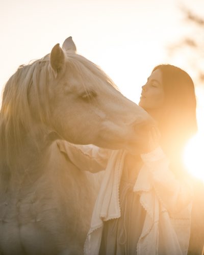 Eine Frau und ein Pferd mit Sonne im Hintergrund